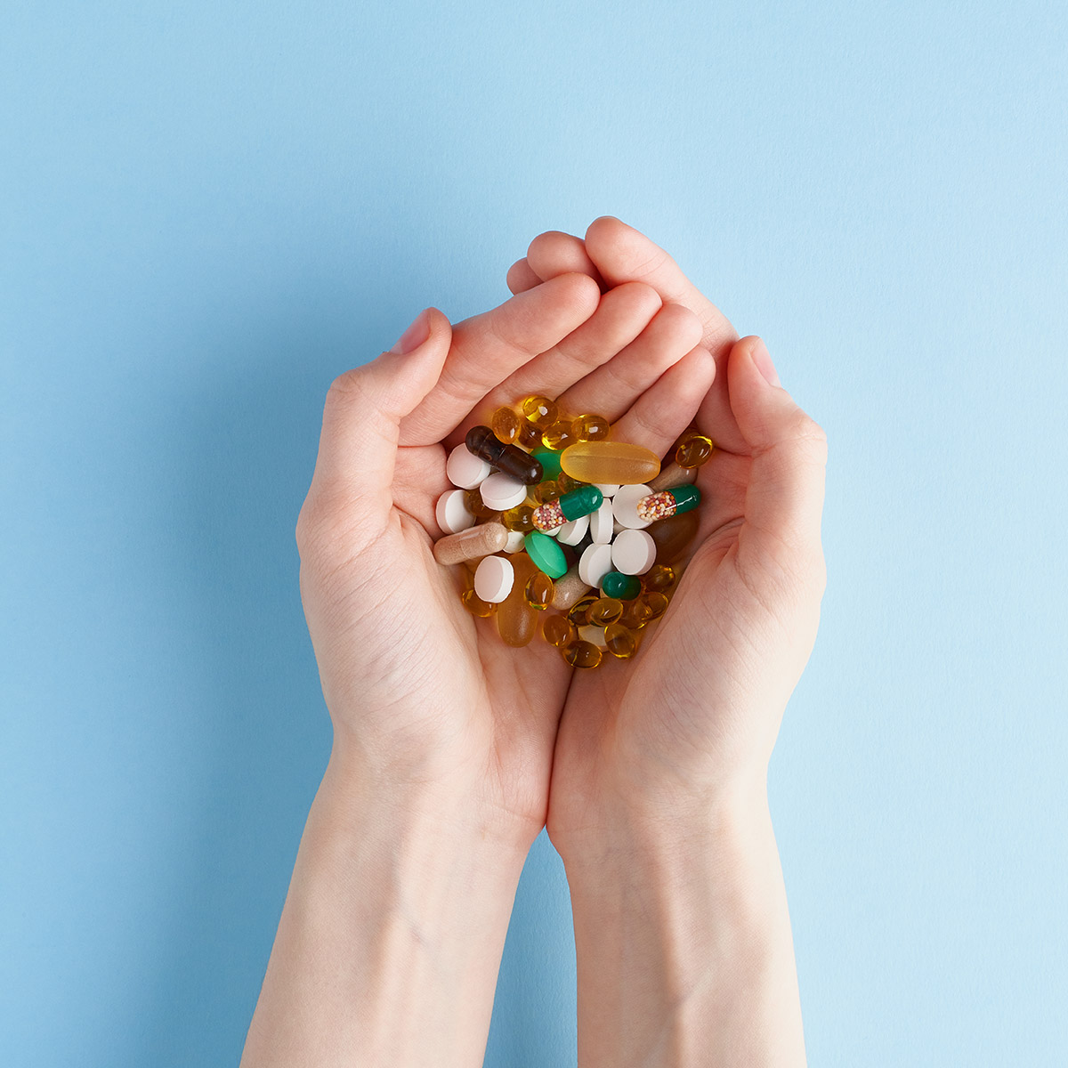 two hands holding many medication pills